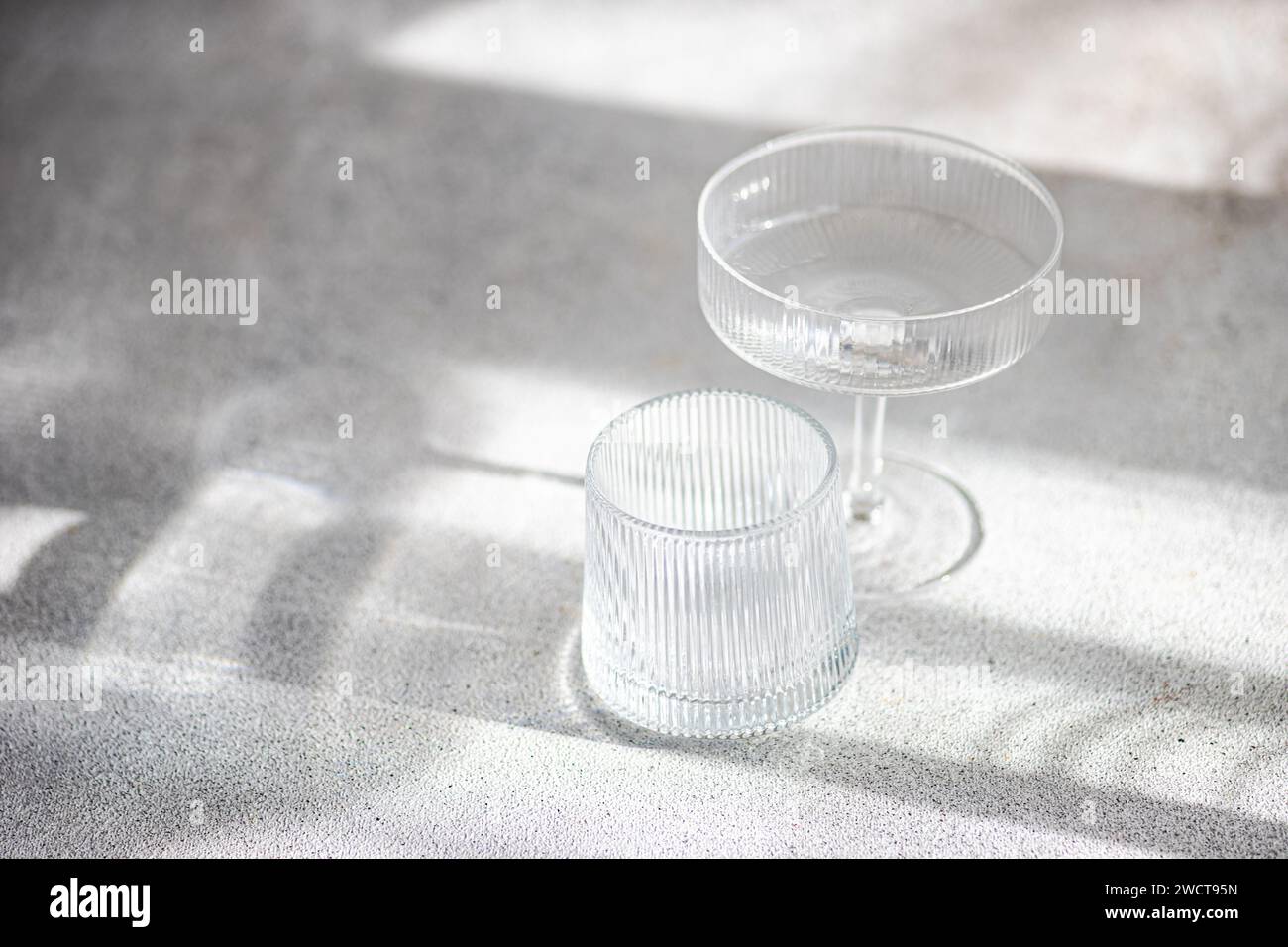 Deux élégantes pièces de verre baignées de lumière douce créant un jeu de lumière et d’ombres sur une surface texturée Banque D'Images