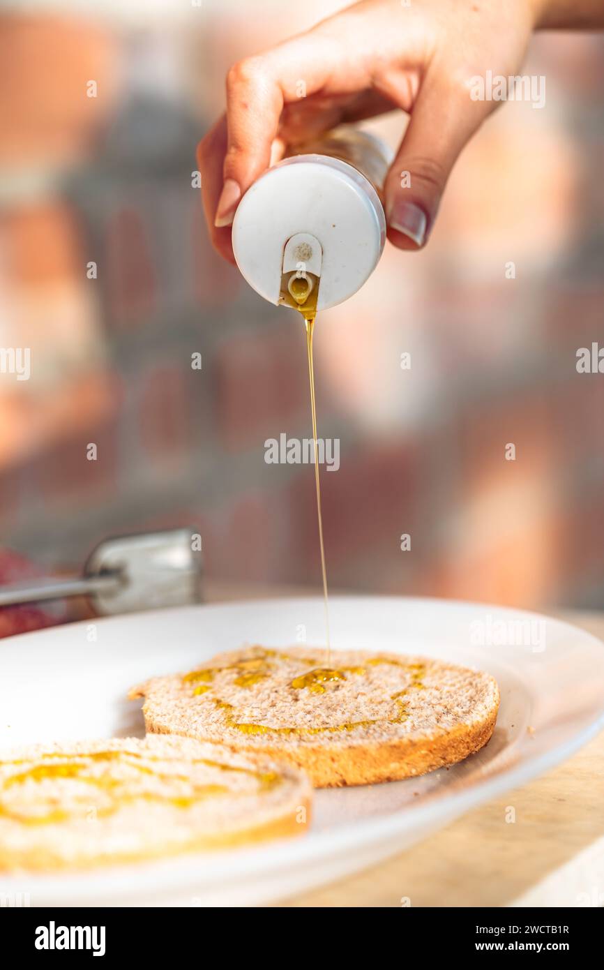 Vue rapprochée de la main versant du miel doré d'un pot sur un pain grillé frais aux grains entiers sur une assiette blanche Banque D'Images