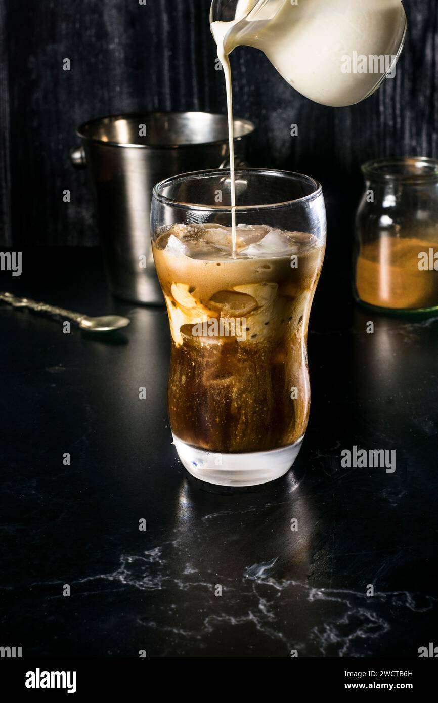 Un verre alléchant de frappe grecque à mi-préparation, avec un jet de lait étant versé, créant un beau tourbillon dans la combinaison de café instantané Banque D'Images