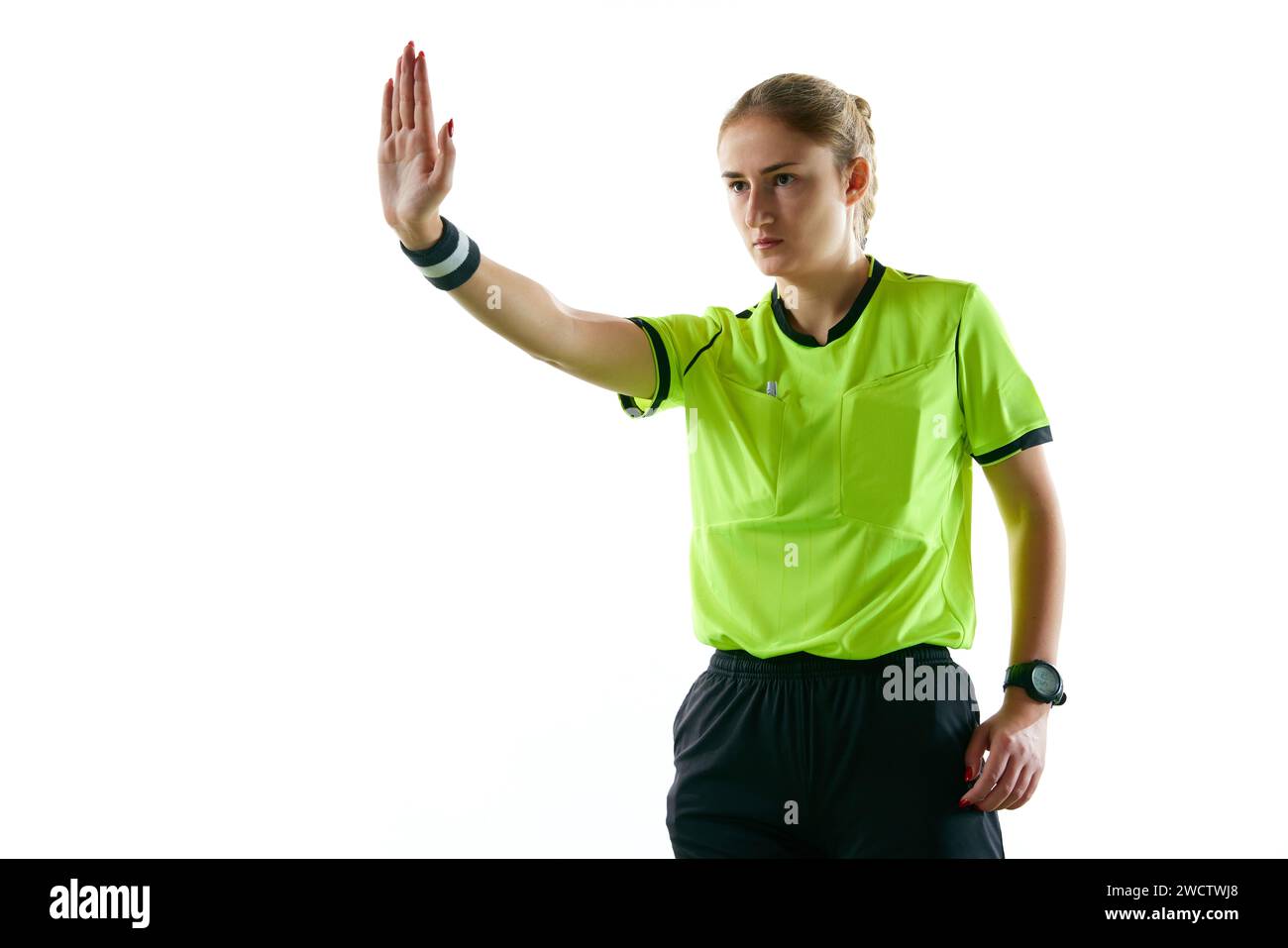 Jeune femme sérieuse, arbitre de football faisant des gestes, levant la main vers l'avant signifiant coup de pied de pénalité sur fond blanc de studio Banque D'Images