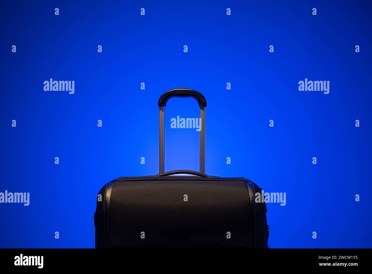 Valise de voyage noir avec poignée de maintien en métal isolé à nouveau fond bleu. Gros plan en studio, pas de gens Banque D'Images