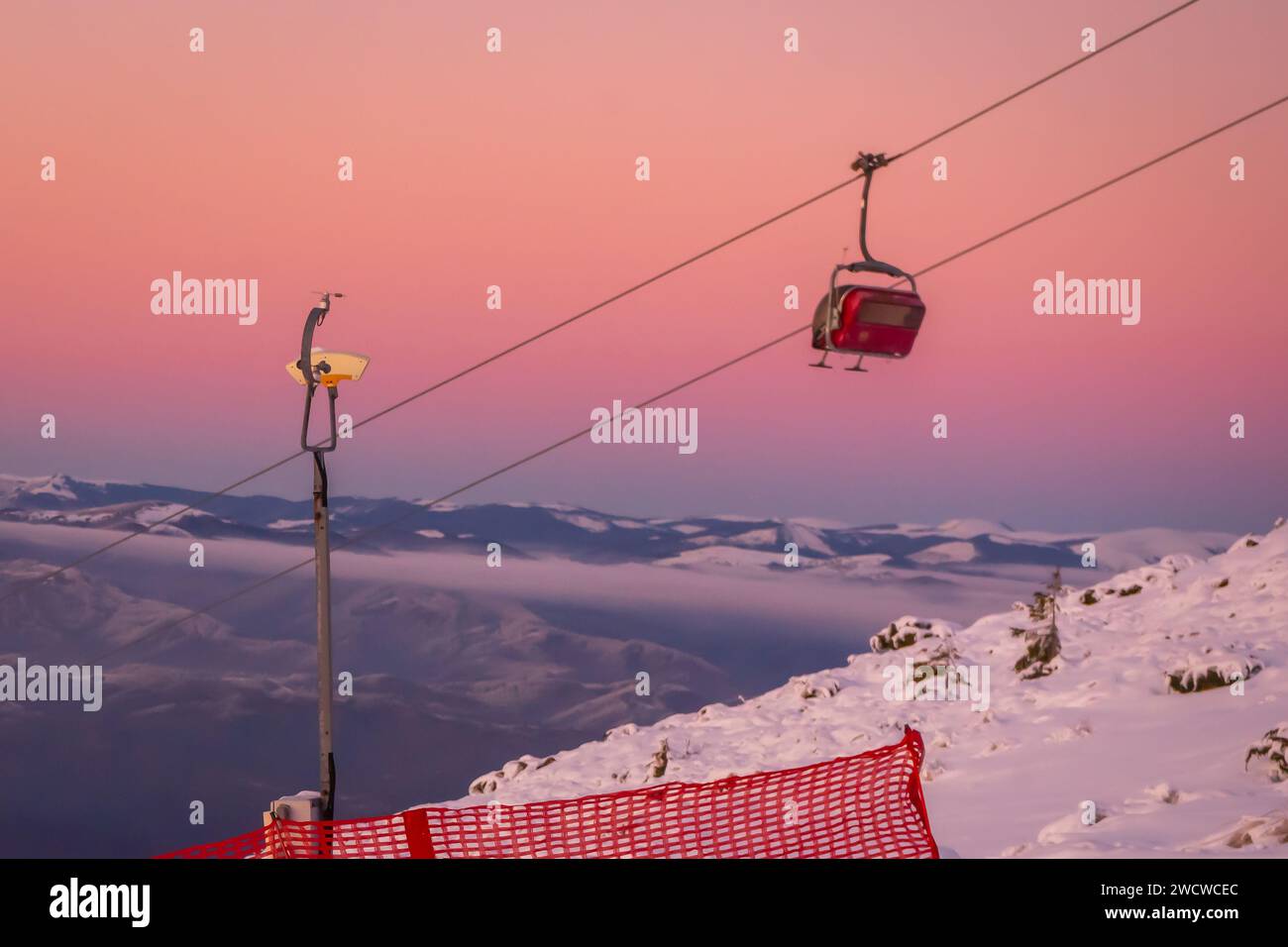 Un magnifique paysage hivernal avec une majestueuse montagne enneigée, ornée d'une remontée mécanique rouge vibrante qui transporte les amateurs de ski et de snowboard. Banque D'Images