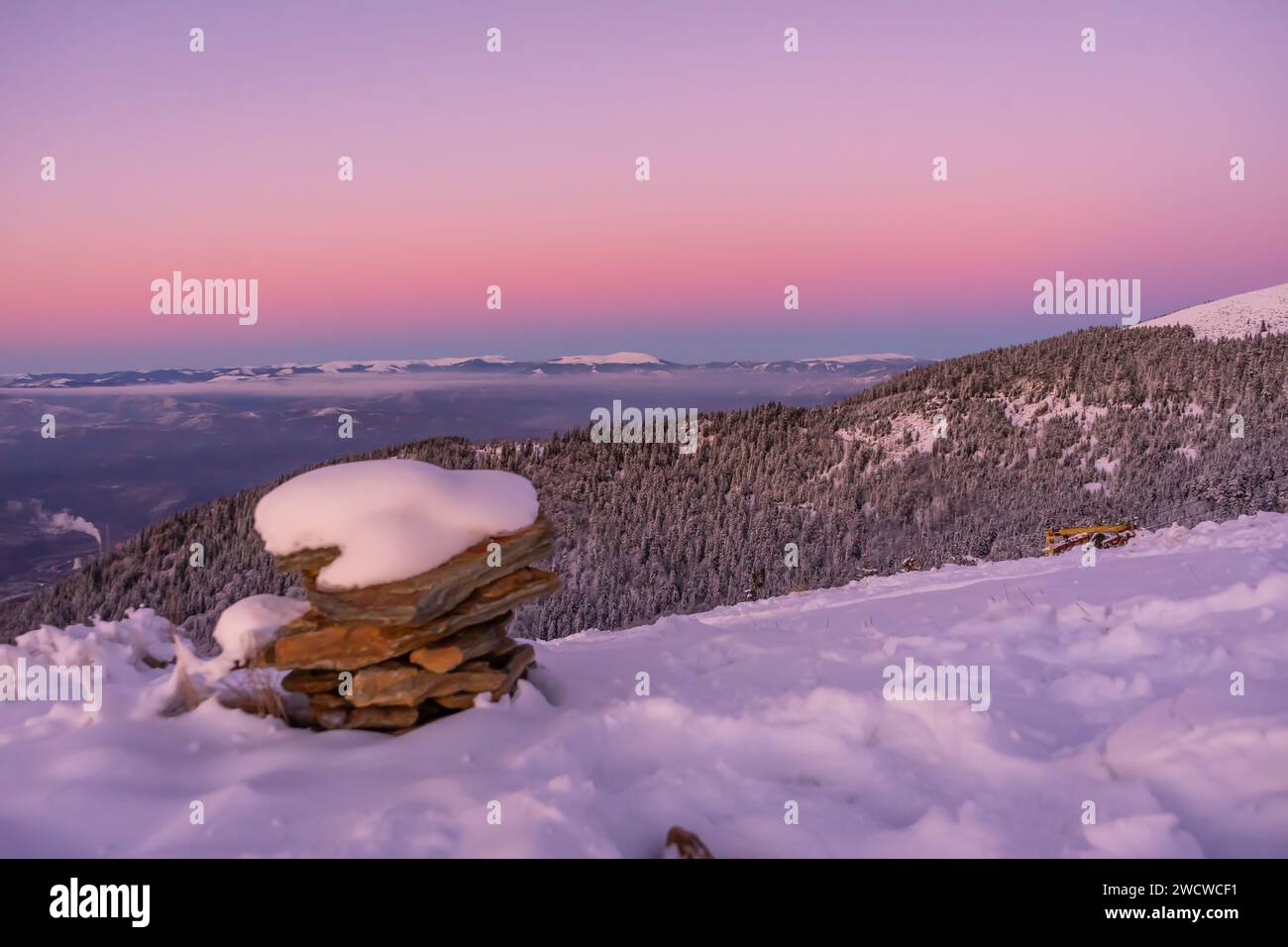 Une belle scène se déroule alors que le soleil se couche derrière une colline enneigée, illuminant un tas serein de rochers perchés au sommet Banque D'Images