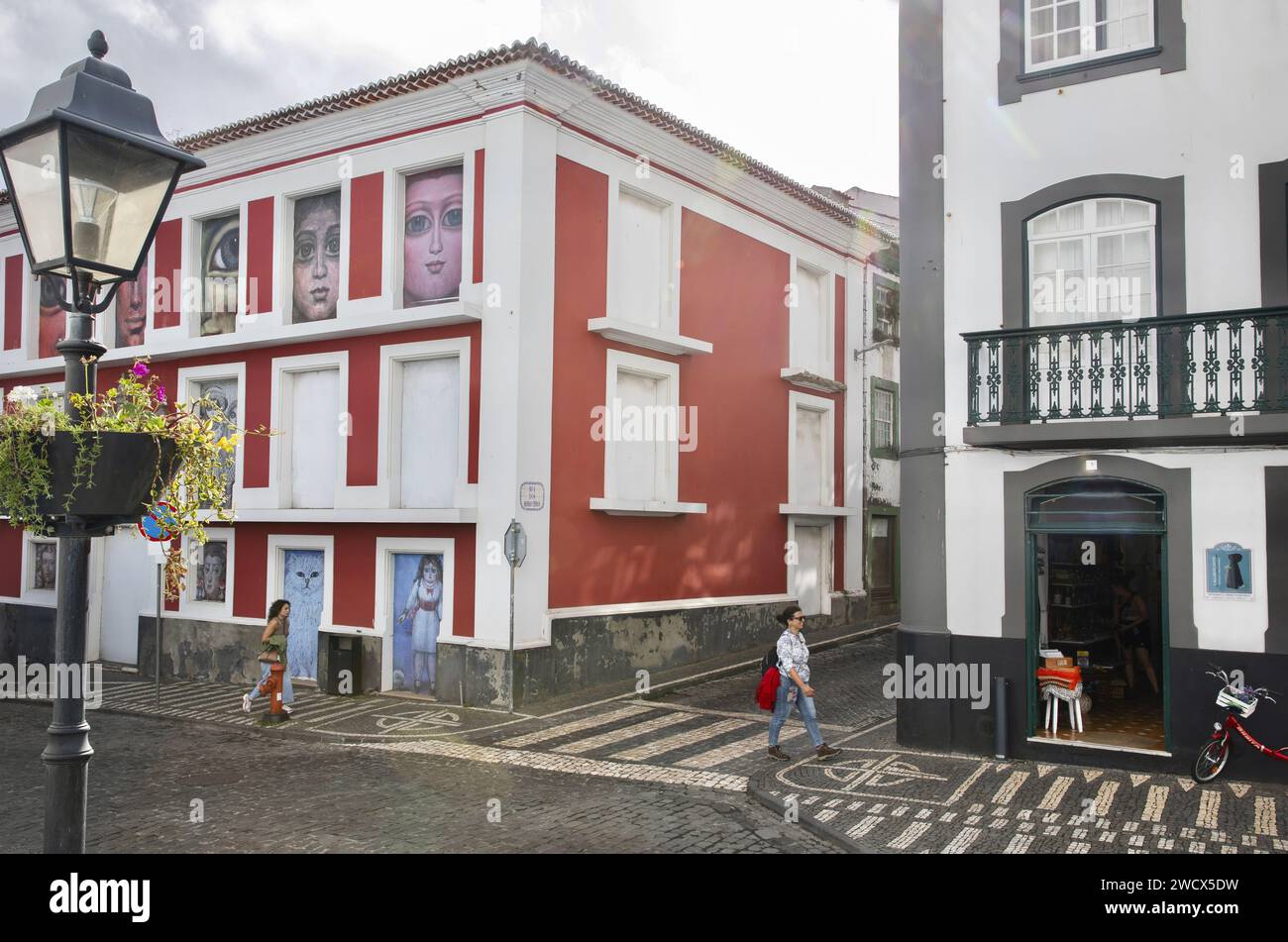 Portugal, archipel des Açores, île de Terceira, Angra do Heroismo, femme marchant dans une ruelle pavée dans le centre historique parmi les bâtiments coloniaux colorés avec des toits de tuiles Banque D'Images
