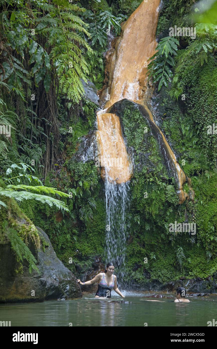 Portugal, archipel des Açores, île de Sao Miguel, Caldera Velha, jeune femme se baignant dans un bassin d'eau chaude sous une cascade entourée d'une végétation exubérante Banque D'Images