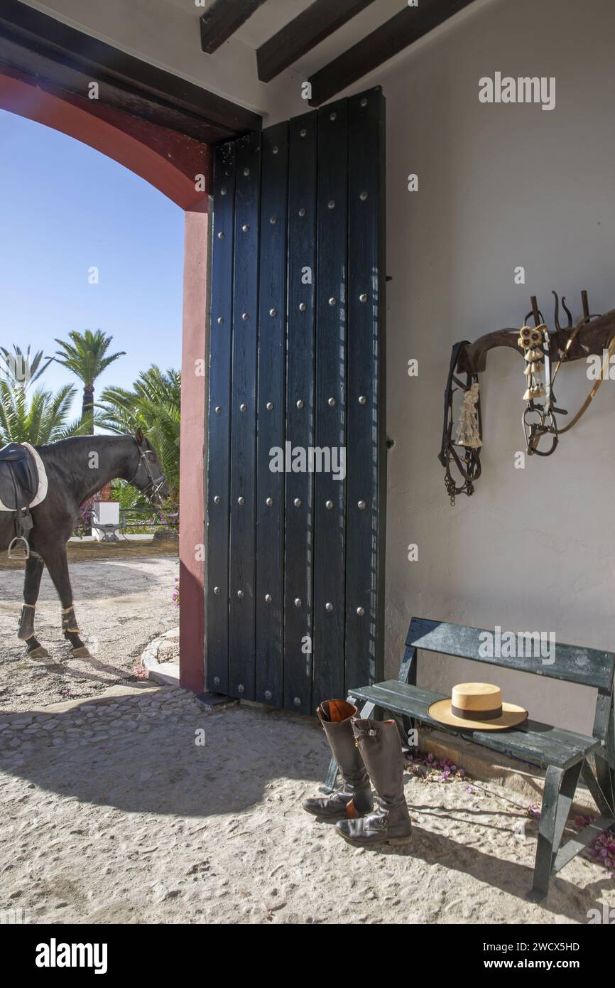 Espagne, Andalousie, Moron de la Frontera, Hacienda las Alcabalas, bottes, chapeau et matériel d'équitation dans le vestibule d'une Hacienda andalouse avec un cheval noir à l'extérieur Banque D'Images