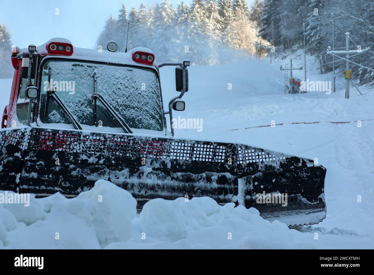 Ratrack répand la neige sur le fond d'un canon à neige, tandis que la neige pulvérise, le soleil brille sur les arbres en arrière-plan. Banque D'Images