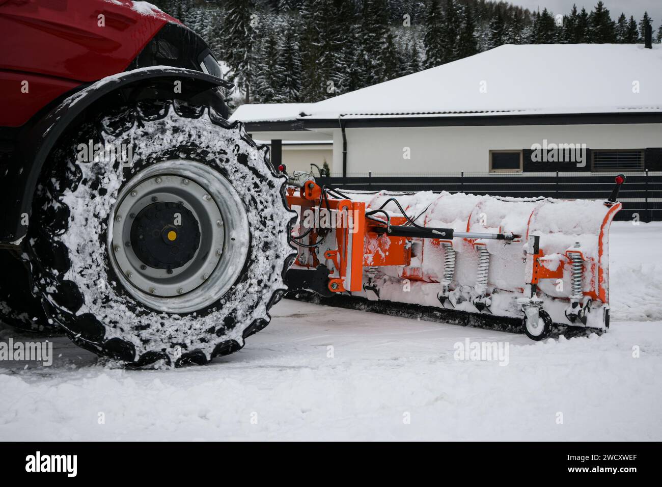 le tracteur rouge pelle la neige après une tempête de neige avec une charrue, vue rapprochée. Banque D'Images