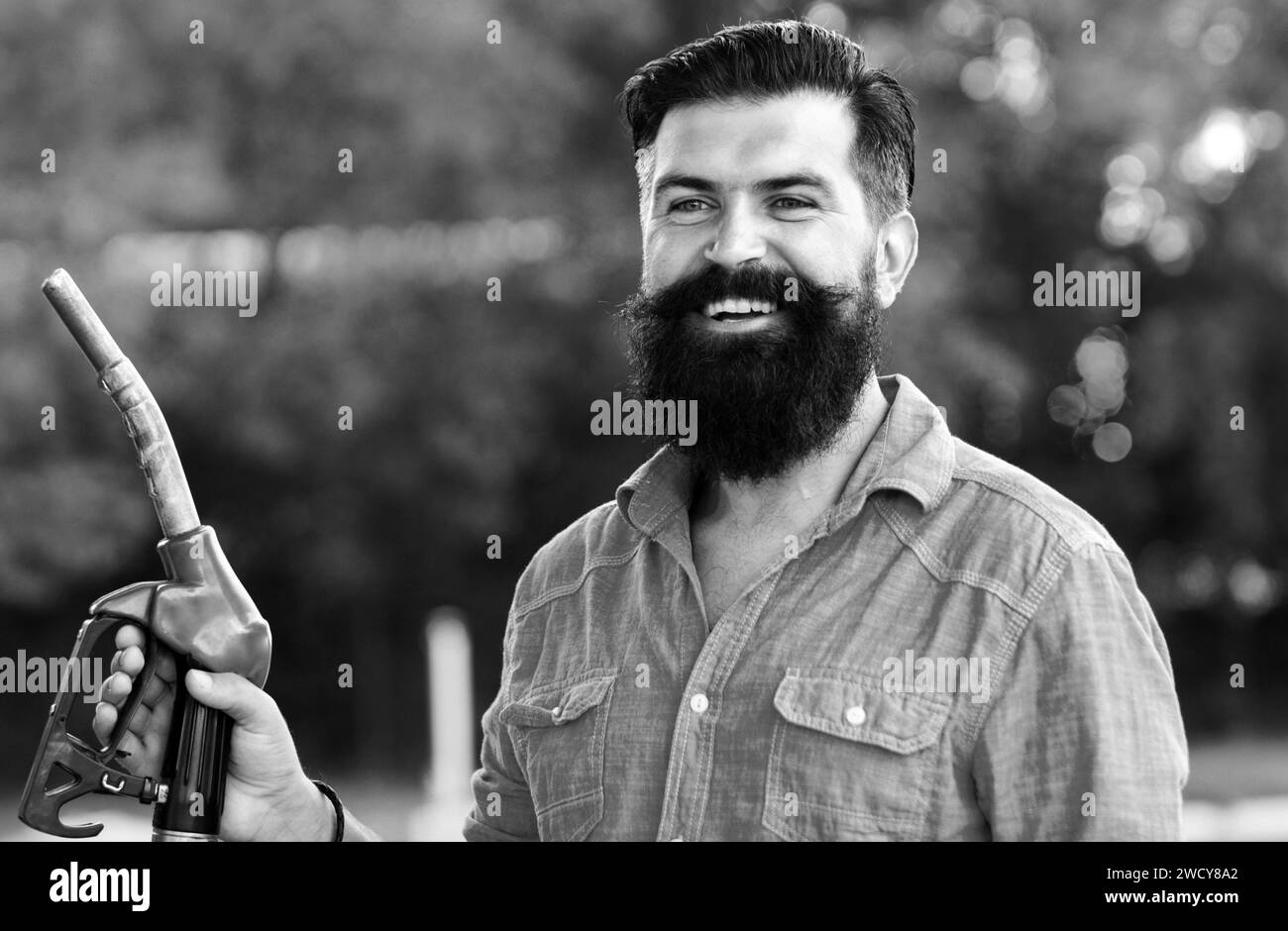 Homme sur les buses de remplissage de la pompe à essence. Station-service. Portrait de l'homme barbu tenir la buse de carburant essence, pompe à carburant. Banque D'Images