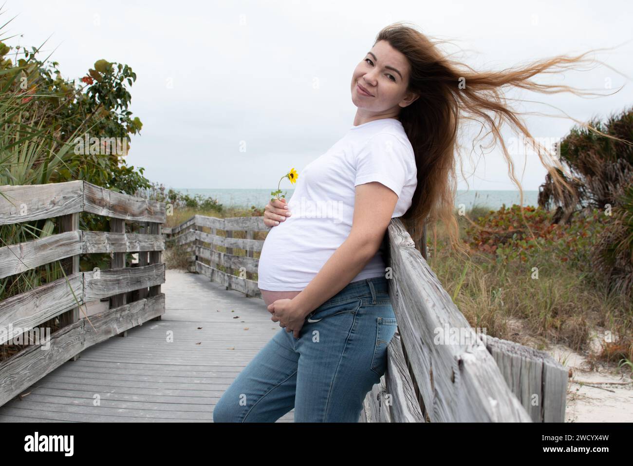 Heureuse femme caucasienne enceinte avec une fleur tenant sa bosse de bébé. Grossesse du troisième trimestre Banque D'Images