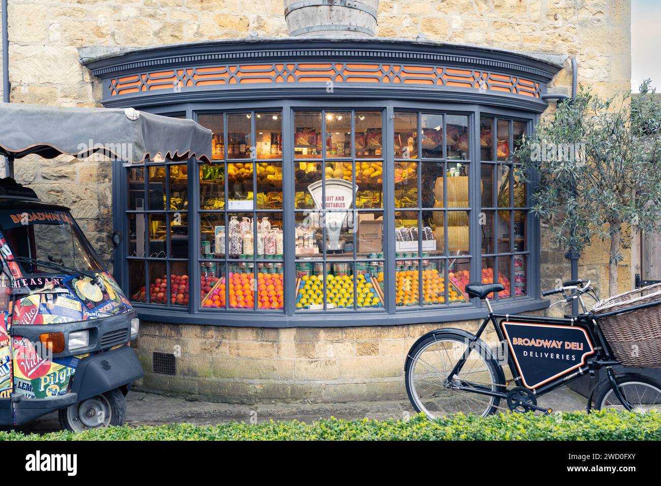 Fruits et légumes et une balance à l'ancienne dans la fenêtre du Broadway Deli, avec un vélo de livraison à l'extérieur. Broadway, Angleterre Banque D'Images