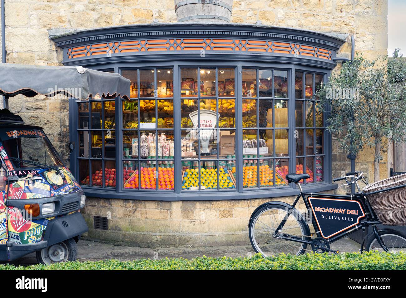Fruits et légumes et une balance à l'ancienne dans la fenêtre du Broadway Deli, avec un vélo de livraison. Broadway, les Cotswolds, Angleterre Banque D'Images