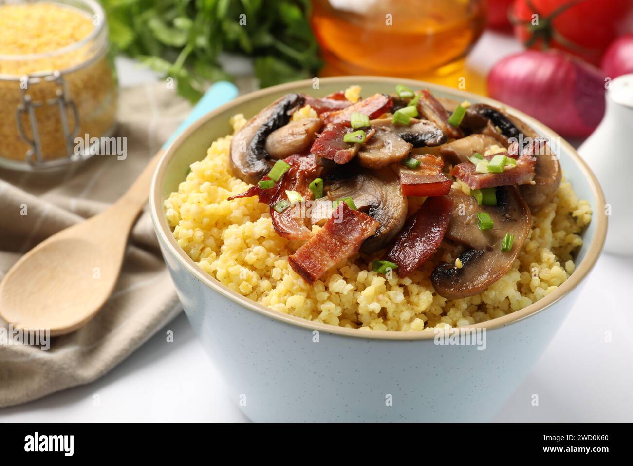 Savoureux porridge de millet avec des champignons, du bacon et de l'oignon vert dans un bol sur une table blanche, gros plan Banque D'Images