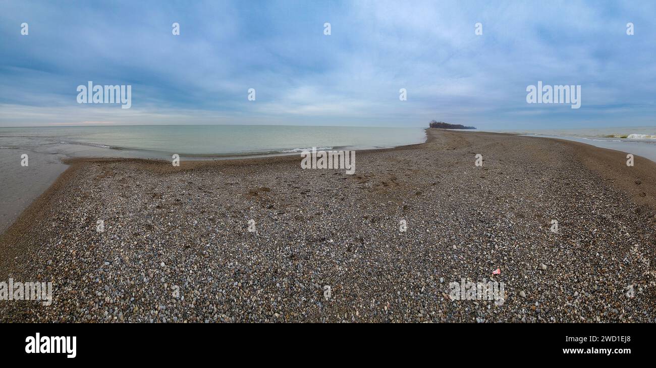 Une scène côtière sereine avec un objet rouge solitaire au milieu d'un rivage sablonneux, avec de l'eau et des cailloux Banque D'Images