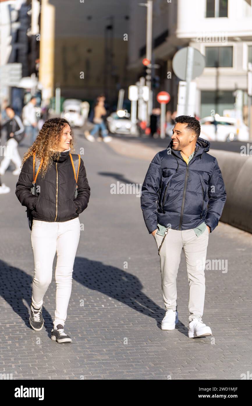Deux amis habillés de façon décontractée pour le temps frais engagent la conversation tout en marchant sur un trottoir animé de la ville. Banque D'Images