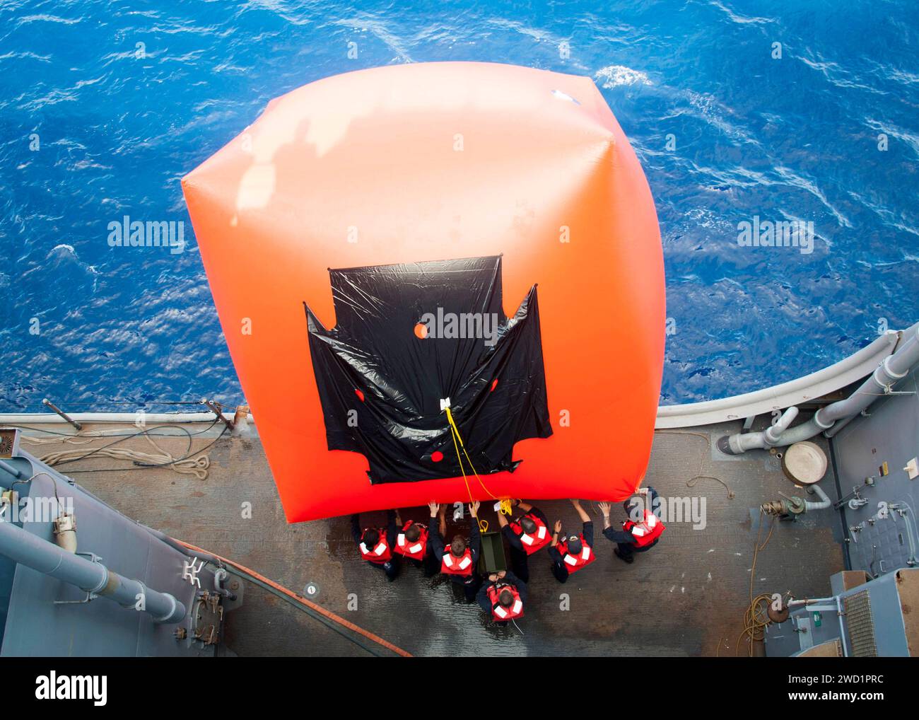 Les aileurs travaillent ensemble pour pousser une cible Killer Tomato par-dessus bord lors d'un exercice de tir réel à bord de l'USS Rushmore. Banque D'Images