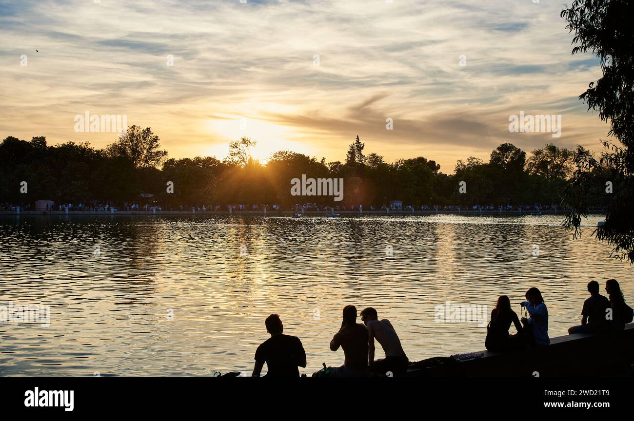 Les gens se refroidissent près de l'étang du parc El Retiro au coucher du soleil dans la capitale espagnole. Les gens assis au bord du lac dans le Parque de El Retiro. Madrid, Espagne Banque D'Images