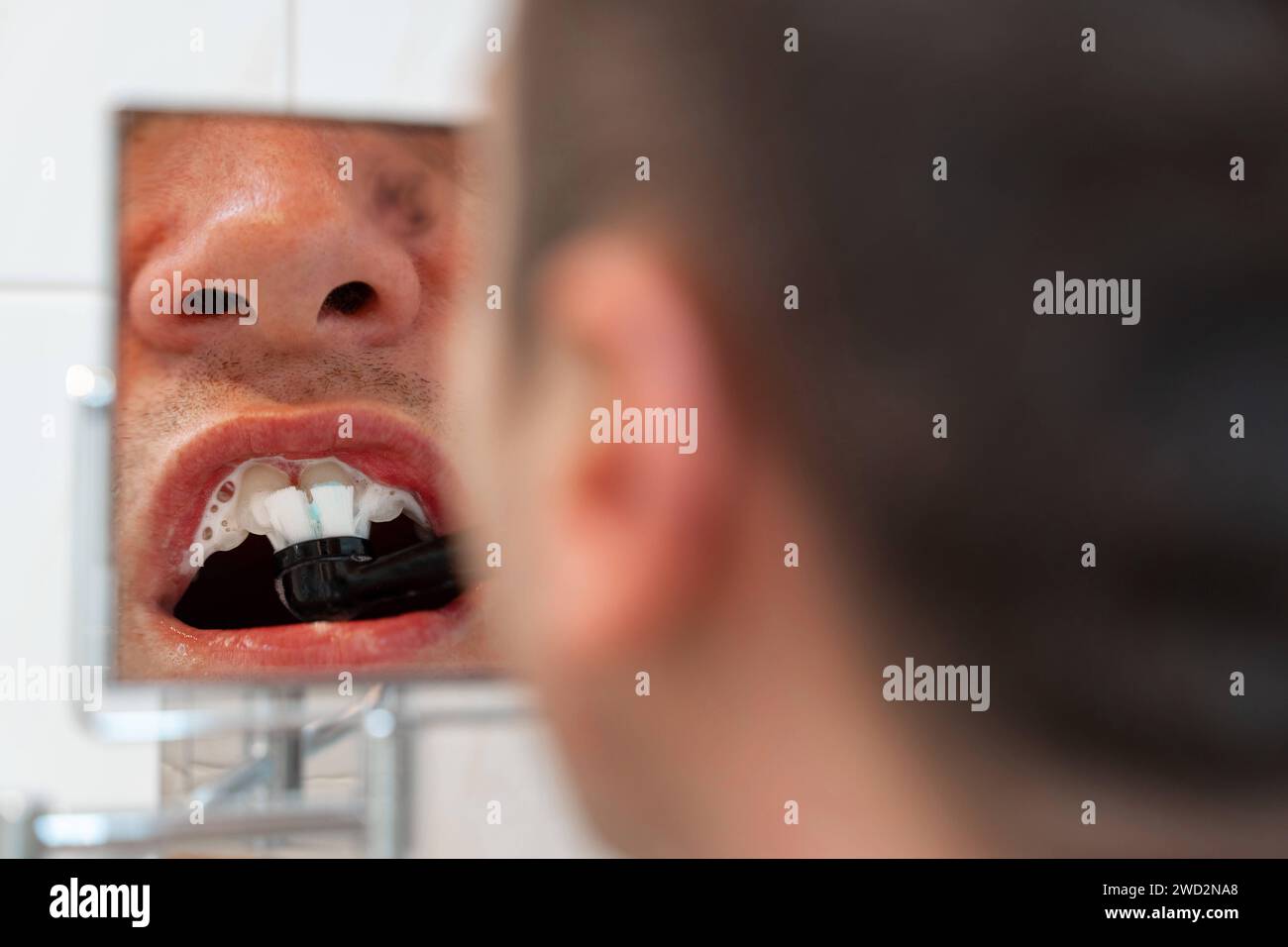 Bavière, Allemagne - 6 janvier 2024 : gros plan d'un homme se brossant les dents avec une brosse à dents électrique devant un miroir cosmétique dans la salle de bain *** Nahaufnahme von einem Mann beim Zähneputzen mit einer elektrischen Zahnbürste vor einem Kosmetikspiegel im Bad Banque D'Images