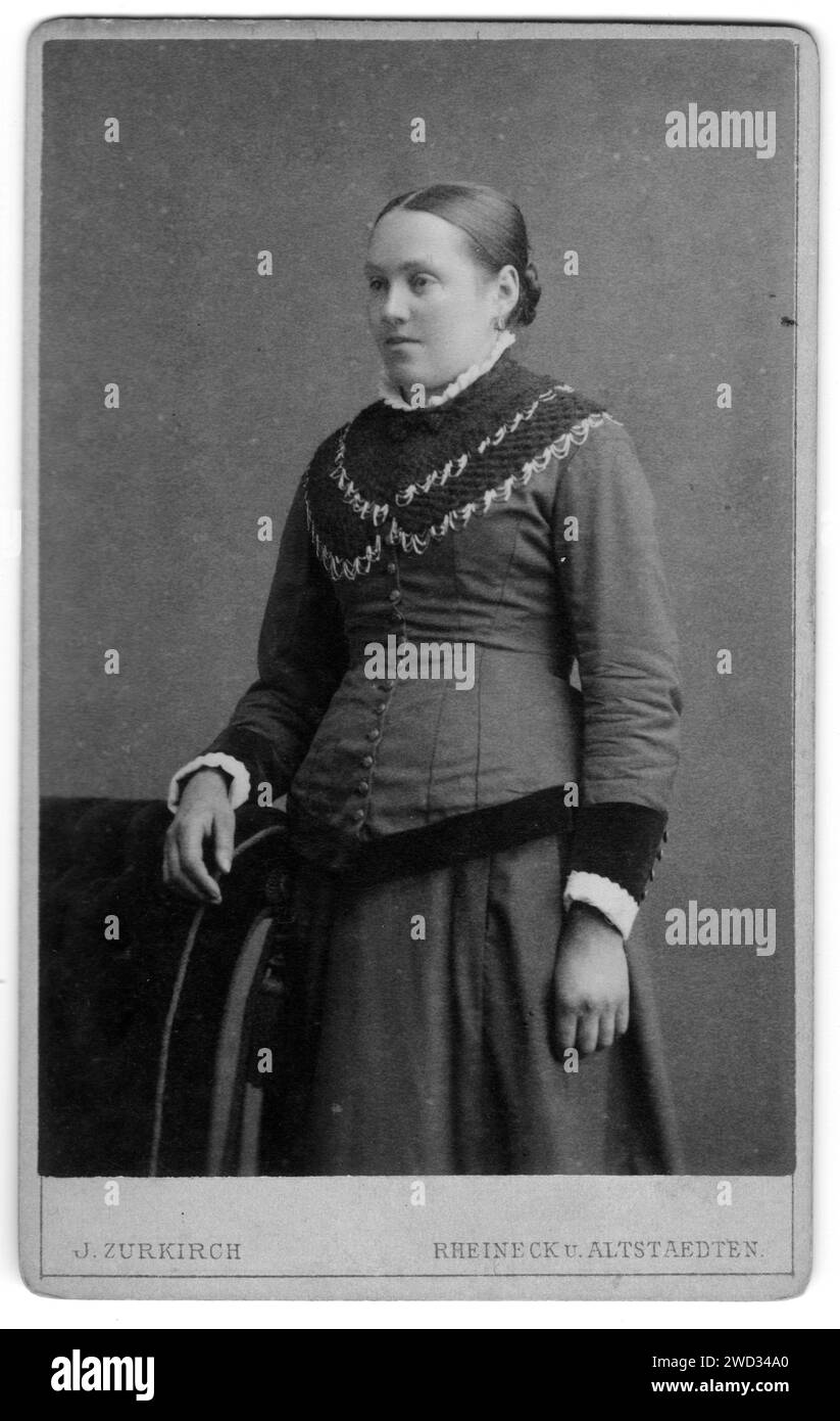 Portrait en studio d'une jeune femme peignée lisse dans un costume debout près d'un fauteuil, studio photographique J. Zurkirch, Rheineck, canton de St. Gal Banque D'Images