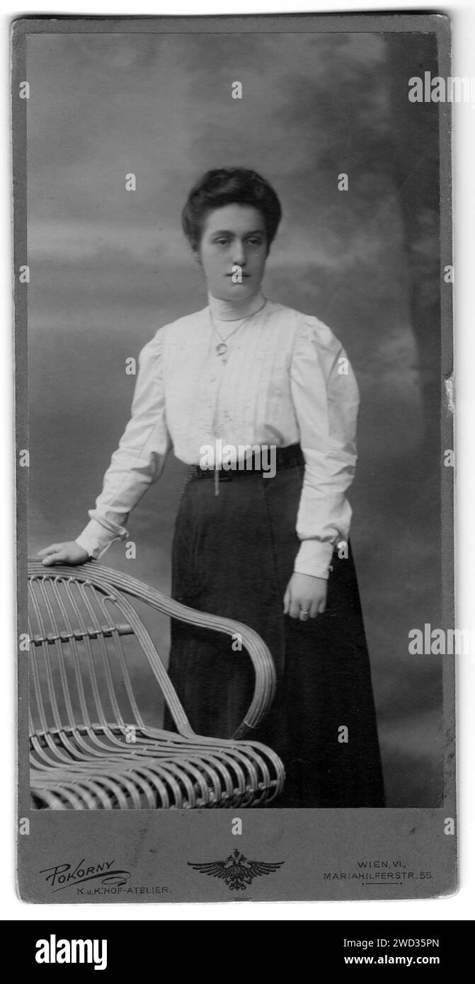 Portrait en studio d'une jeune belle femme dans un chemisier blanc et jupe sombre, appuyé sur le dos d'une chaise en osier. Le studio photo de Pokorny. Vienne, au Banque D'Images