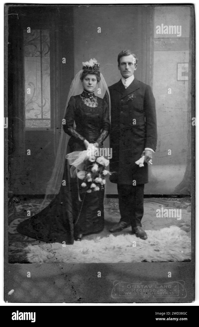 Portrait en pied de jeunes mariés en studio. La mariée a un voile sur la tête et tient un bouquet de roses blanches dans ses mains. Le marié porte Banque D'Images
