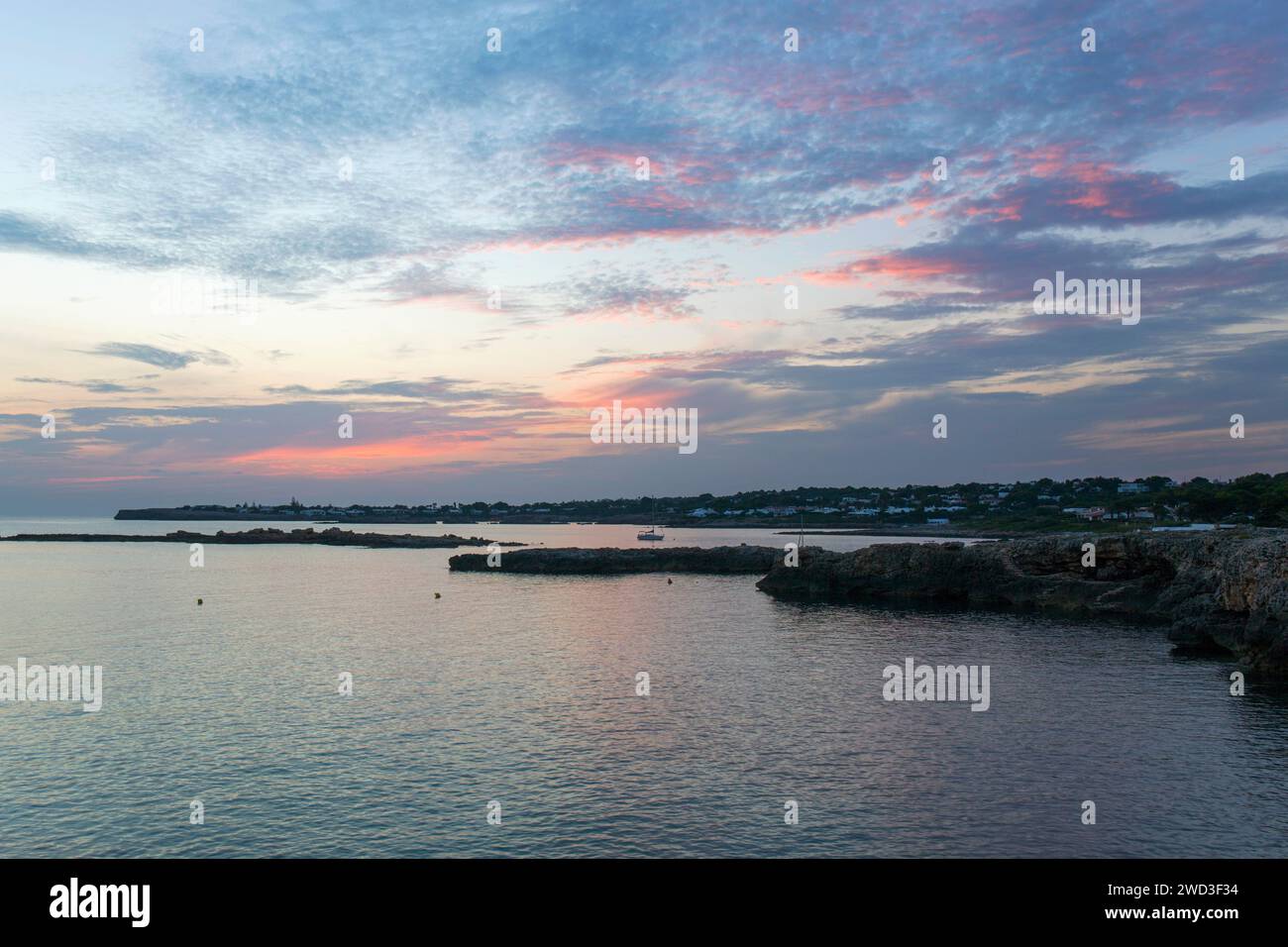 Binibèquer Vell, Minorque, Îles Baléares, Espagne. Vue le long de la côte rocheuse après le coucher du soleil, nuages roses dans le ciel. Banque D'Images