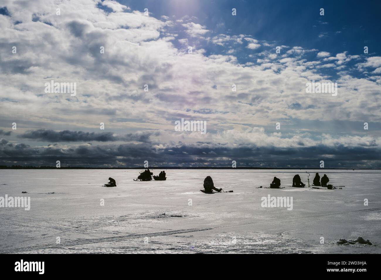 silhouettes de pêcheurs pêchant et motoneige en hiver sur la glace de la rivière sous le ciel nuageux bleu jour de gel Banque D'Images
