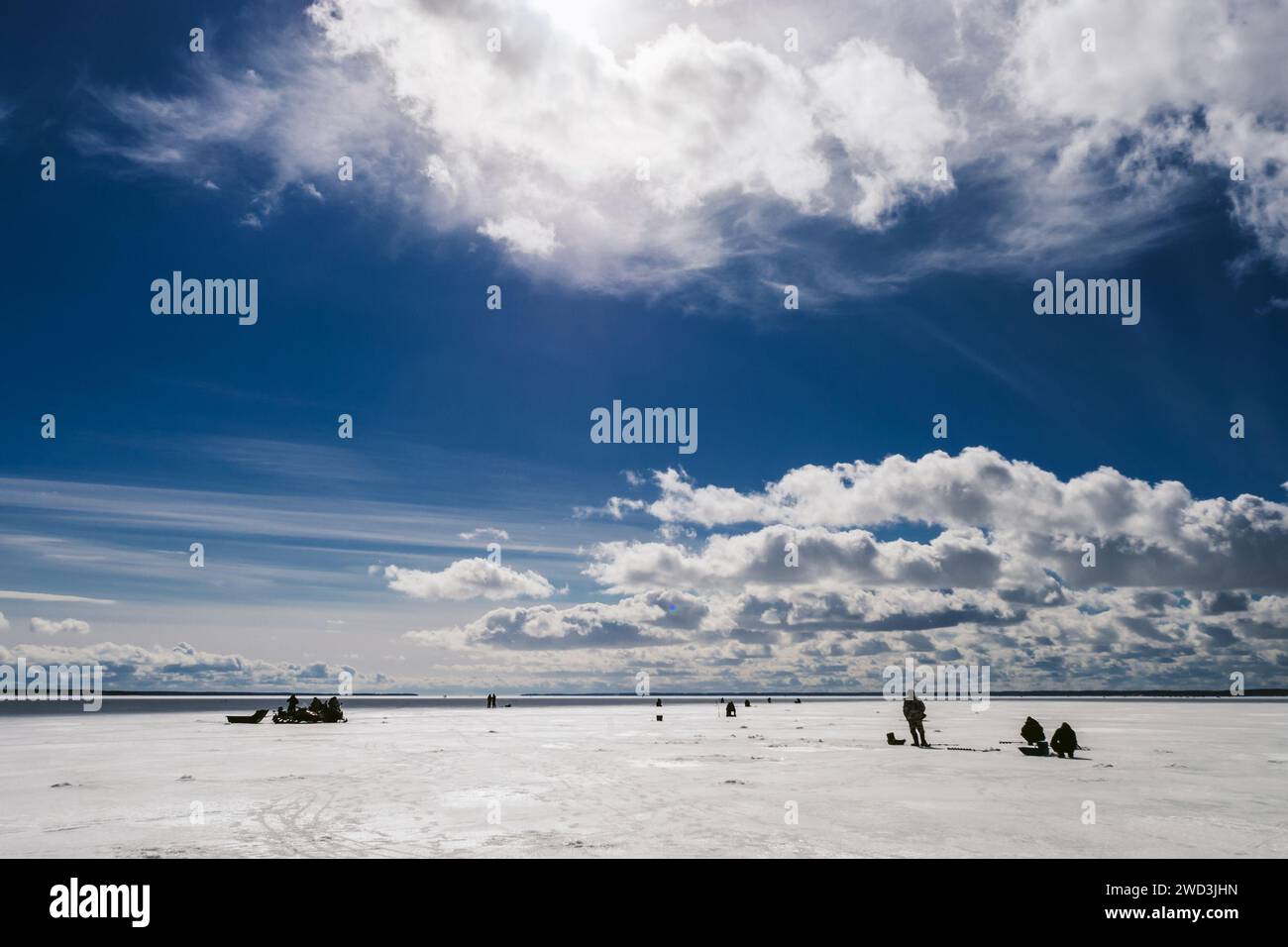 silhouettes de pêcheurs pêchant et motoneige en hiver sur la glace de la rivière sous le ciel nuageux bleu jour de gel Banque D'Images