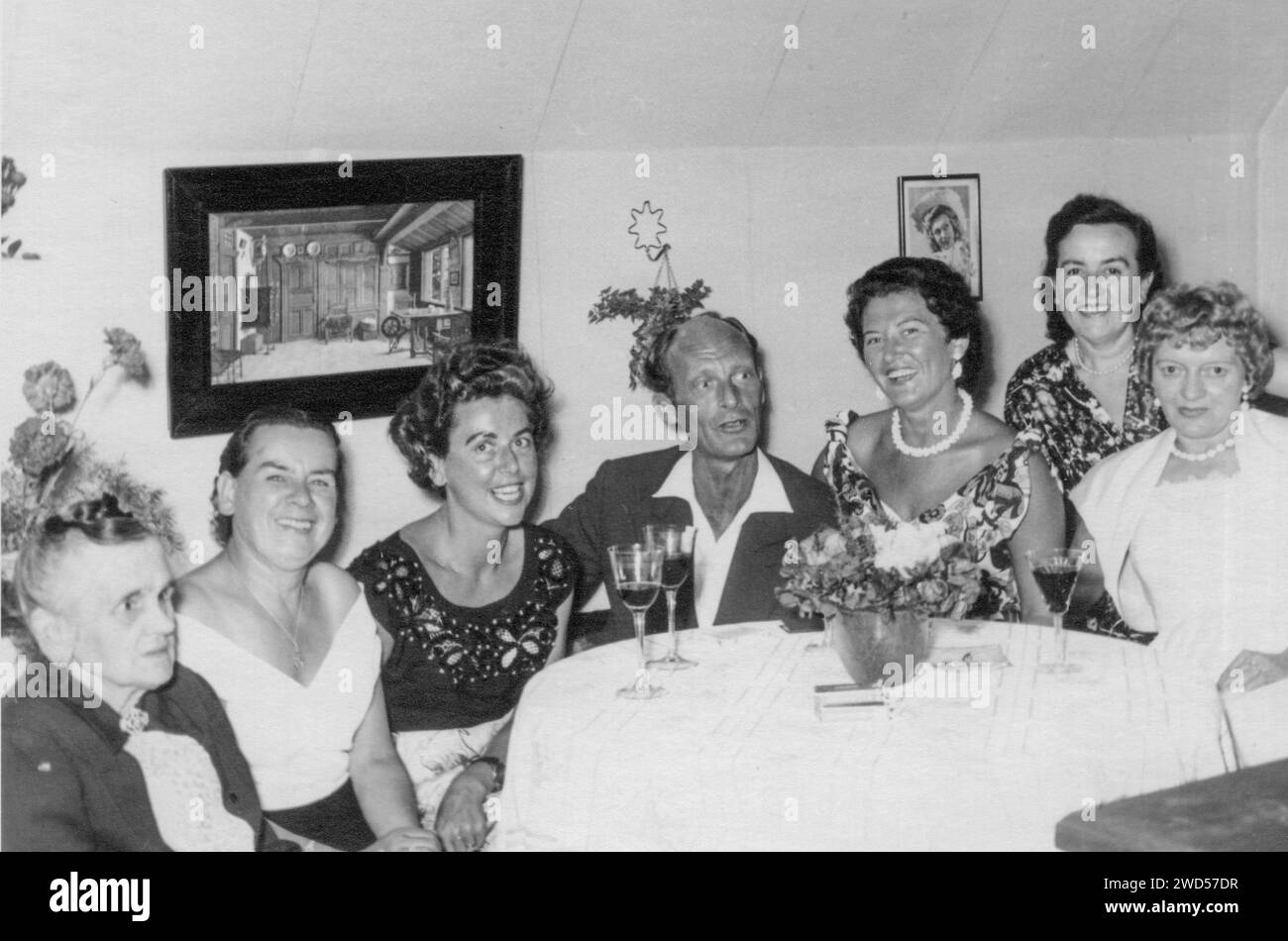 Une photo antique avec montre une compagnie de six femmes et un homme assis devant une table ronde recouverte d'une nappe blanche, verres de vin stand i. Banque D'Images