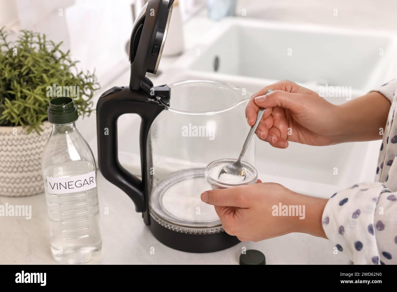 Femme ajoutant du bicarbonate de soude dans une bouilloire électrique dans la cuisine, closeup Banque D'Images