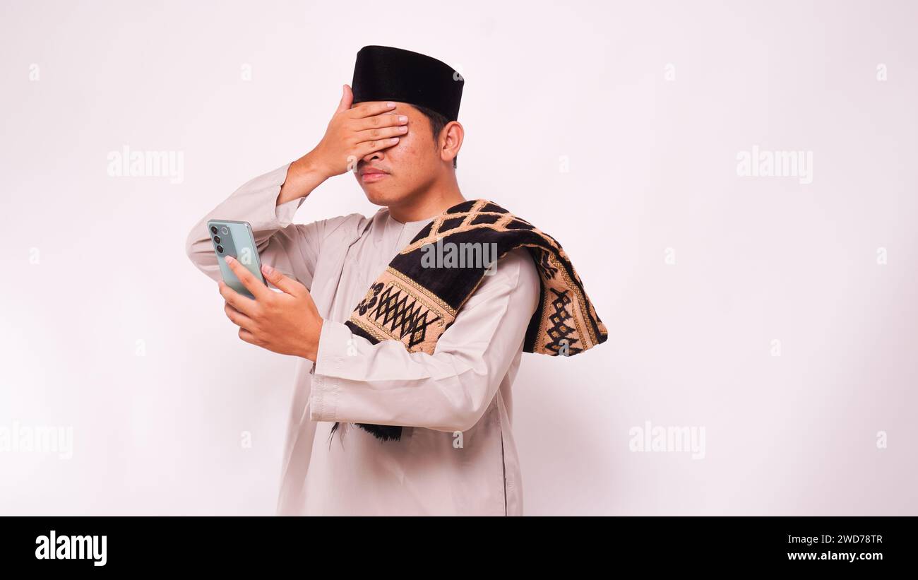Homme musulman asiatique couvrant ses yeux en regardant smartphone pendant le ramadan. isolé sur fond blanc Banque D'Images