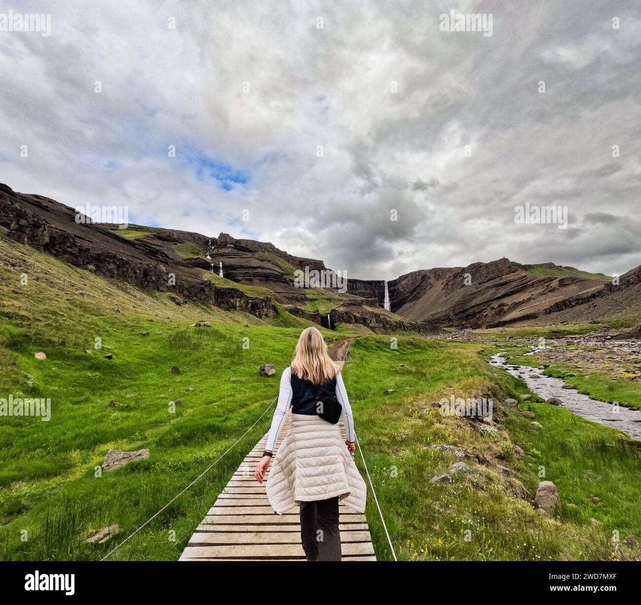 Femme marche le long du chemin à travers les champs d'herbe verte à la cascade Banque D'Images