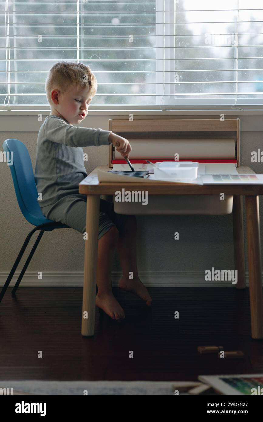 Enfant garçon peinture avec de la peinture aquarelle à la table dans la maison Banque D'Images