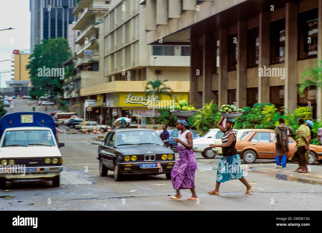 Côte d'Ivoire, Abidjan ; deux femmes avec des paniers remplis de fruits traversant une route. Banque D'Images