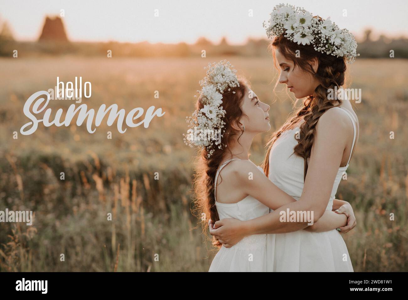 Carte de voeux avec l'inscription Hello Summer. Mère et fille heureuses avec des couronnes de fleurs dans un champ au coucher du soleil. Grain de film ajouté Banque D'Images