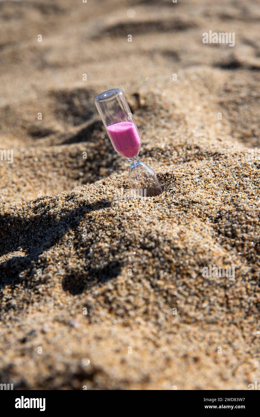 Le sable rose descend gracieusement dans un sablier de bord de mer, capturant des moments fugaces de beauté tranquille sur la plage Banque D'Images