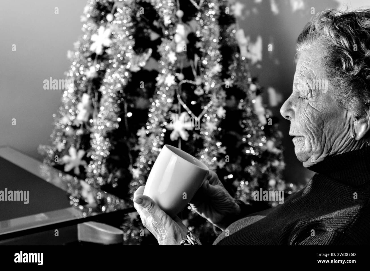 Femme senior tenant une tasse de café chaud avec fond d'arbre de Noël. photographie noir et blanc Banque D'Images