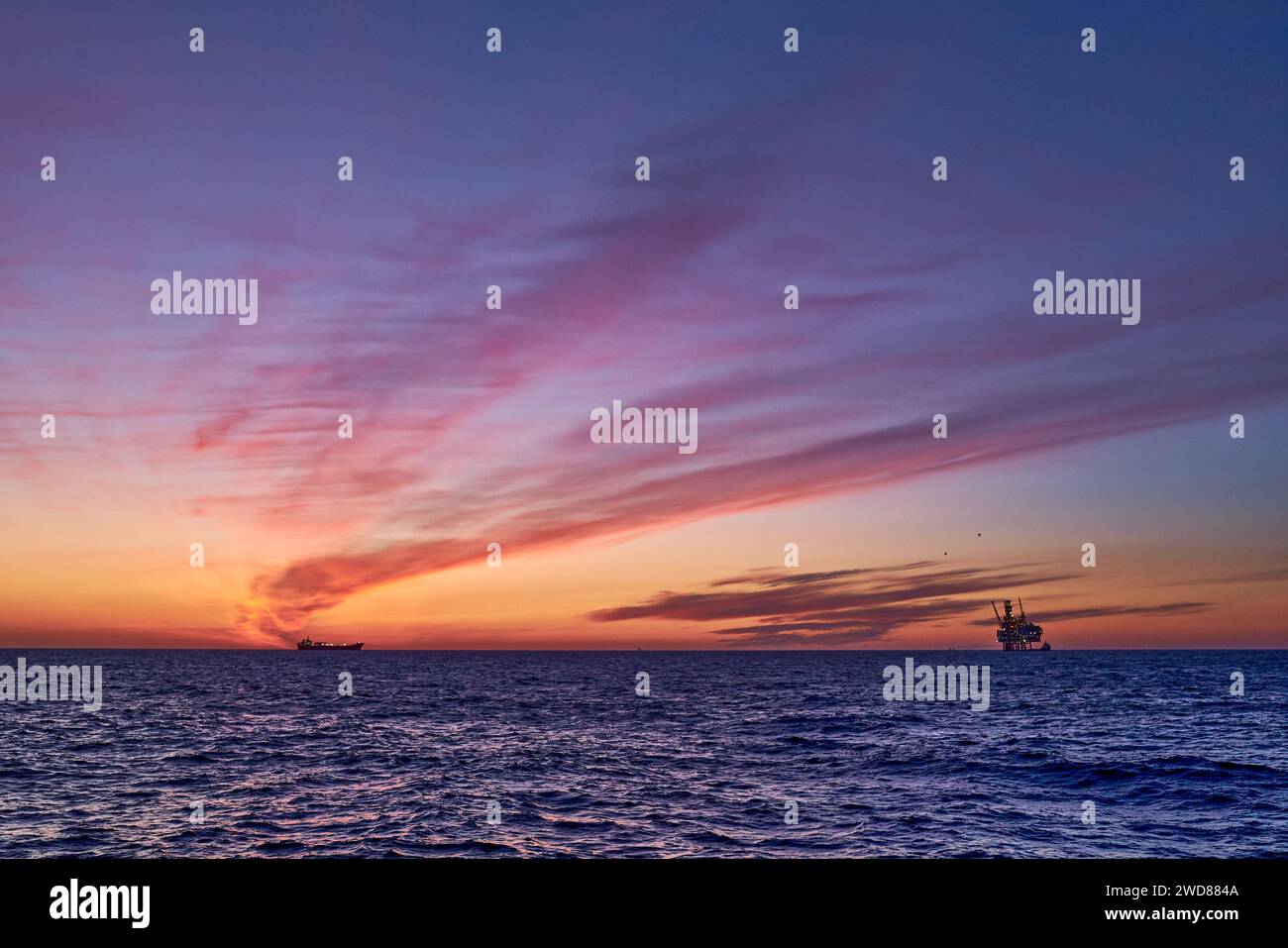 Beau lever de soleil dans la mer avec ciel coloré rose, jaune, orange et violet, océan bleu et silhouette d'une plate-forme de jackup à l'horizon. Banque D'Images