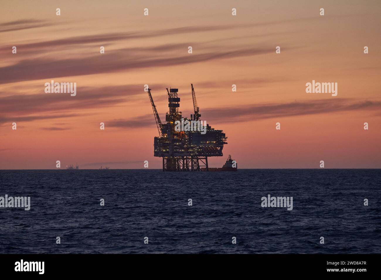 Silhouette d'une plate-forme de forage de cric avec bateau d'approvisionnement à l'horizon lors d'un beau lever de soleil orange dans l'océan. Banque D'Images
