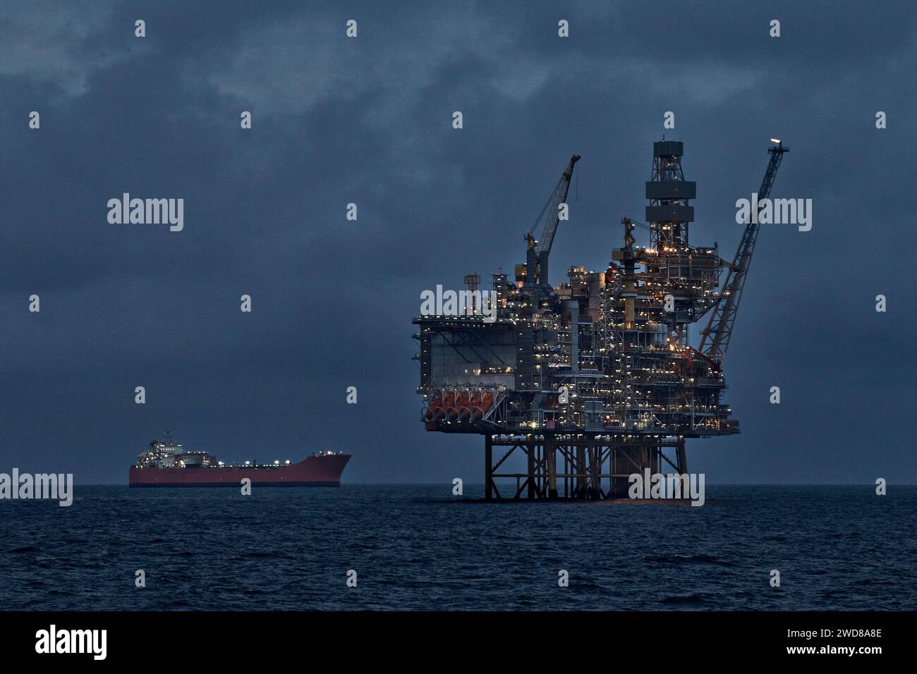 Production de pétrole brut en mer avec engin de forage à jackup et pétrolier de stockage de production flottant la nuit. Banque D'Images