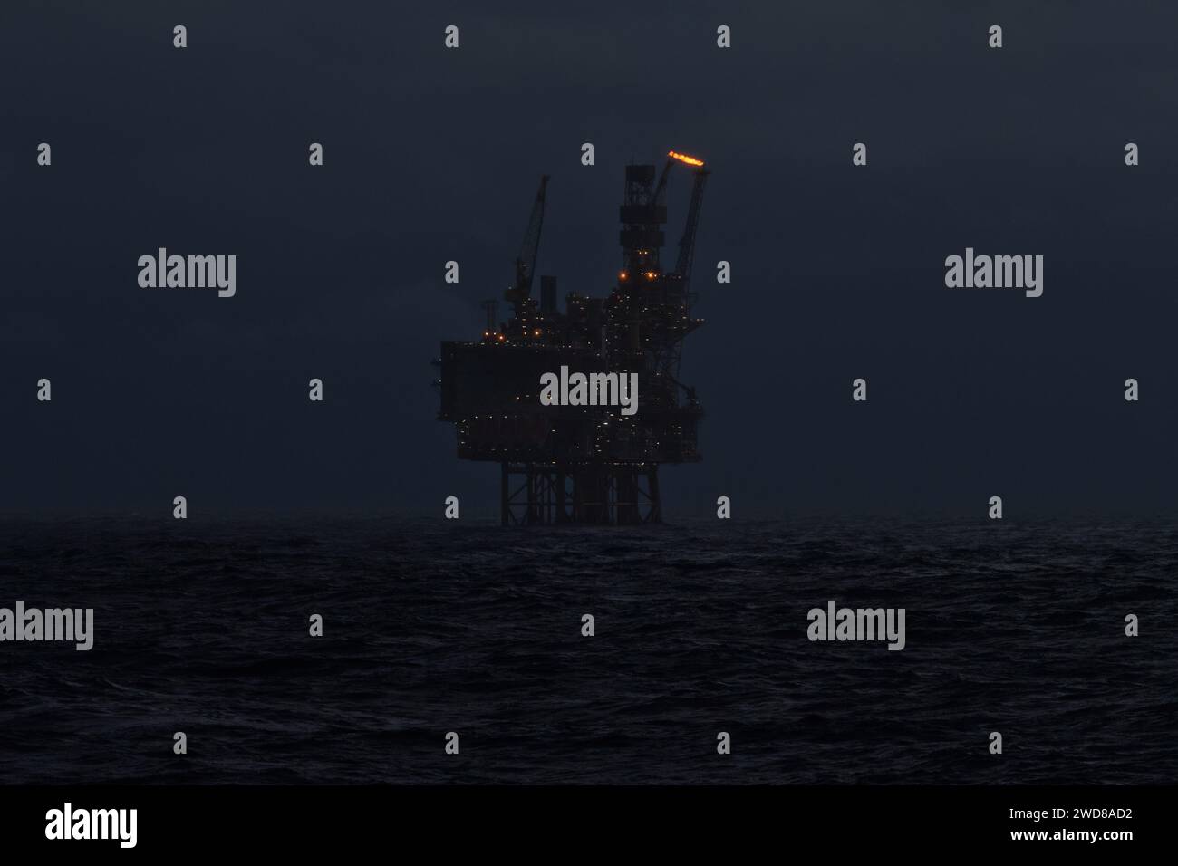 Photo d'une plate-forme de forage pétrolier et gazier offshore en mer la nuit, avec torche de gaz sortant du tuyau. Banque D'Images