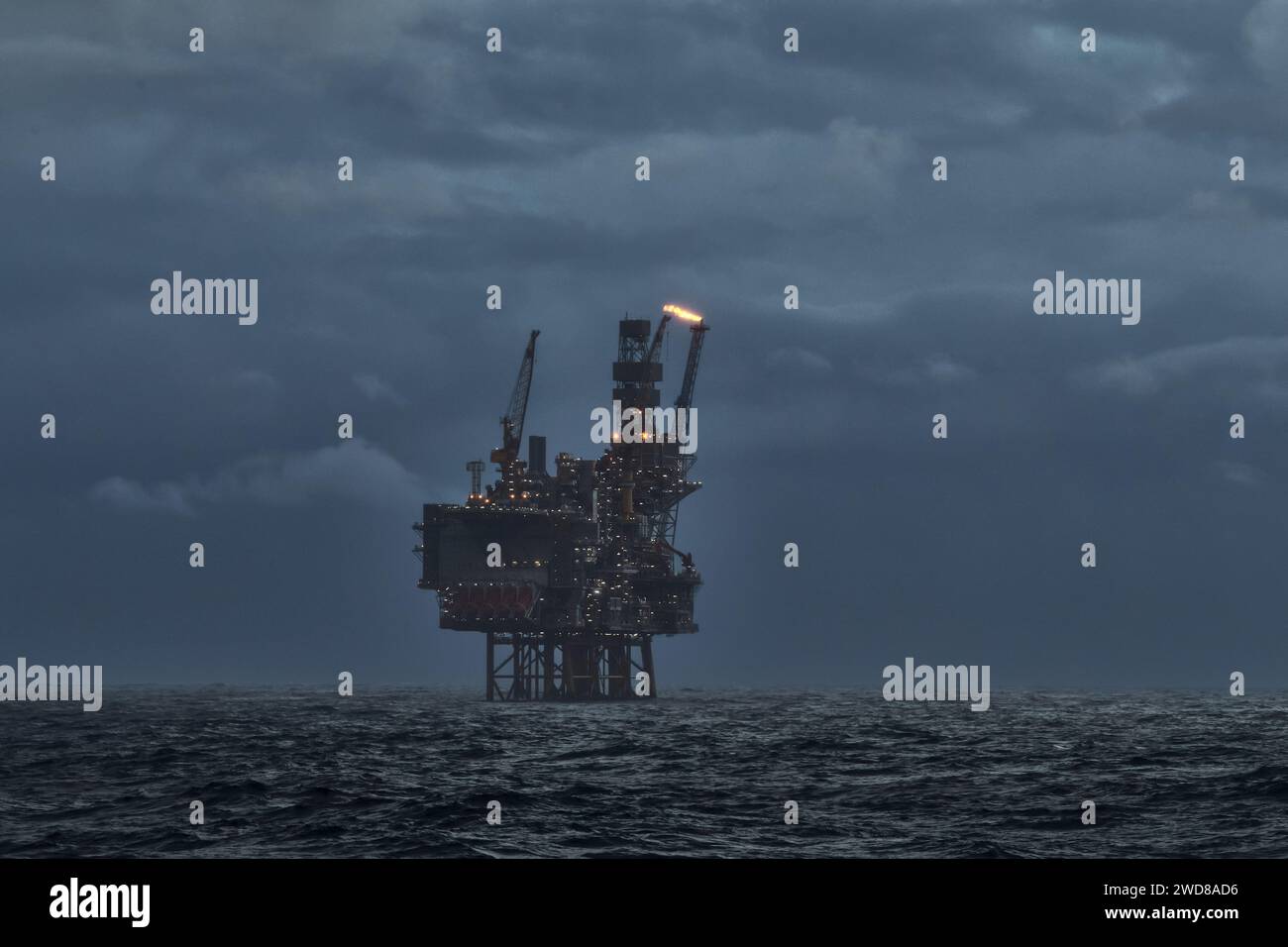 Image d'une plate-forme de forage pétrolier et gazier offshore dans la mer par temps orageux au crépuscule, avec torche de gaz venant du tuyau. Banque D'Images