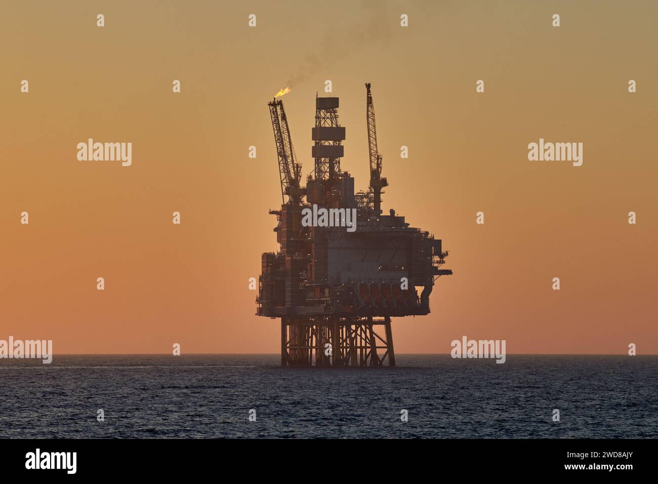 Silhouette de plate-forme offshore de jackup de pétrole et de gaz dans l'océan pendant le coucher du soleil, avec le ciel jaune et l'eau calme. Banque D'Images