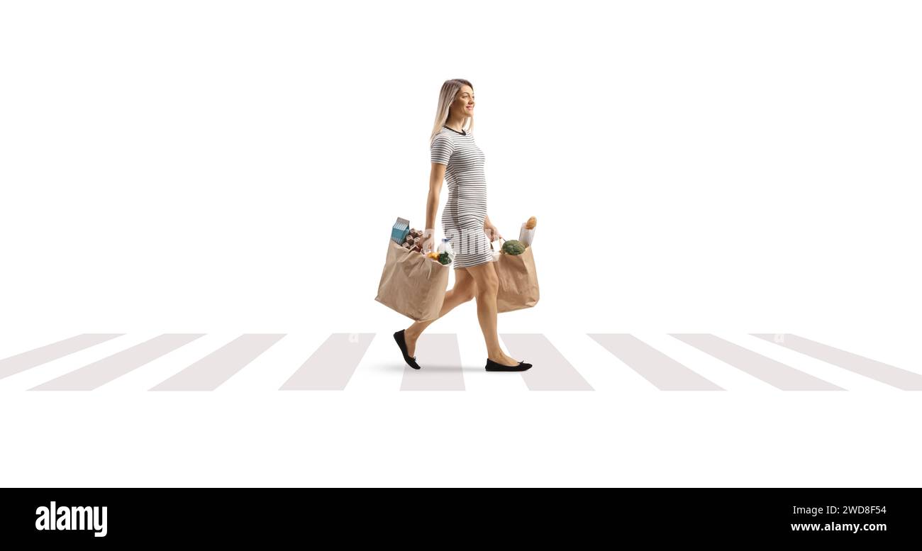 Plan de profil complet d'une jeune femme marchant avec des sacs d'épicerie à un signe zèbre piéton isolé sur fond blanc Banque D'Images