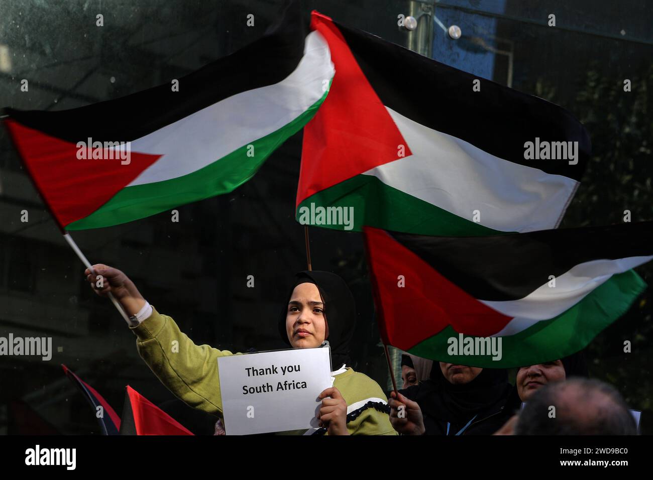 Beyrouth, Liban. 19 janvier 2024. Un réfugié palestinien agite des drapeaux palestiniens tout en portant une pancarte remerciant l’Afrique du Sud, lors d’une manifestation pour remercier l’Afrique du Sud d’avoir déposé une plainte contre Israël devant la Cour internationale de Justice (CIJ) pour génocide à Gaza. Des dizaines de réfugiés libanais et palestiniens se sont rassemblés devant l'ambassade d'Afrique du Sud à Beyrouth pour exprimer leur gratitude pour sa position dans la guerre continue israélo-Hamas dans la bande de Gaza. Crédit : Marwan Naamani/dpa/Alamy Live News Banque D'Images
