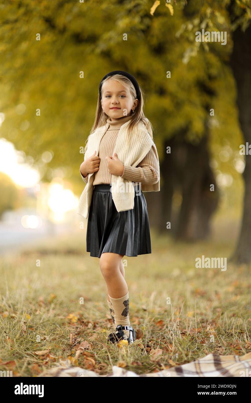 Journée des enfants. Joyeuse petite fille de 5-6 ans posant et souriant à la caméra à l'extérieur debout près de l'arbre au parc d'automne. Presch tendre élégant Banque D'Images