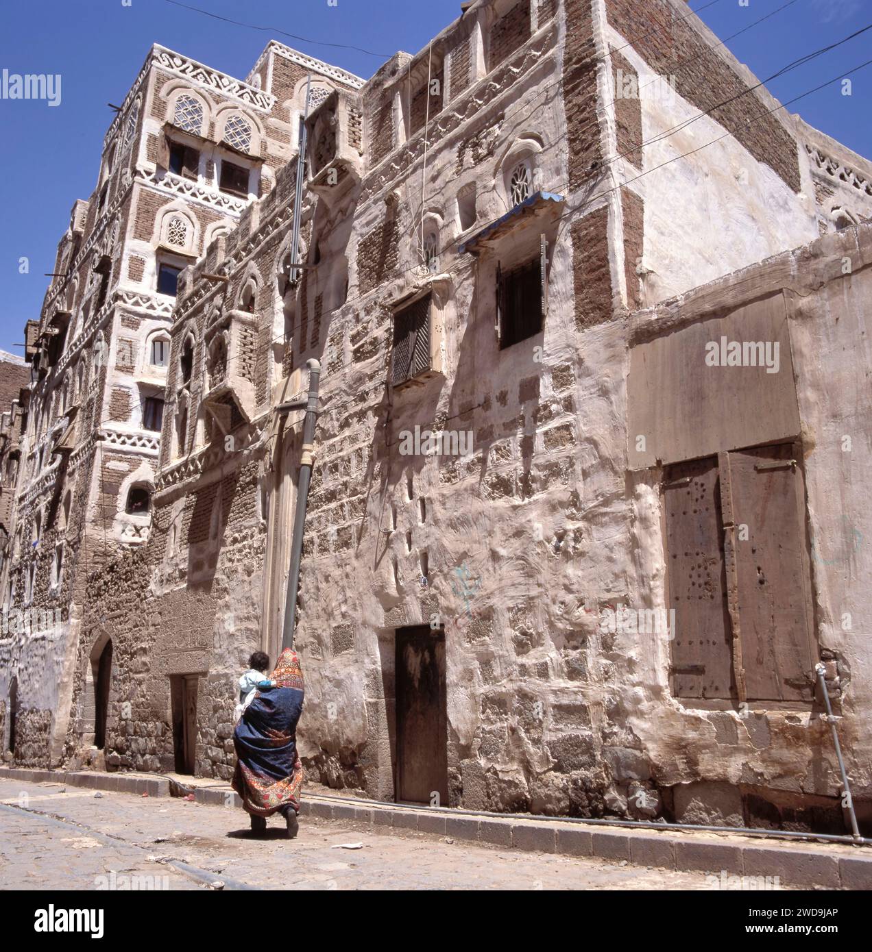 Des femmes voilées marchant avec son enfant dans une rue de Sanaa, capitale du Yémen. Les maisons sont typiques du Yémen Banque D'Images