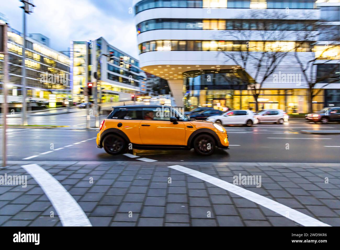 Innerstädtische Straße mit Fahrzeugen, moderne Architektur am Abend. Bewegungsunschärfe. BMW Mini. // 17.01.2024 : Stuttgart, Bade-Württemberg, Deutschland. *** Rue de la ville avec des véhicules, architecture moderne dans le soir mouvement flou BMW Mini 17 01 2024 Stuttgart, Baden Württemberg, Allemagne Banque D'Images