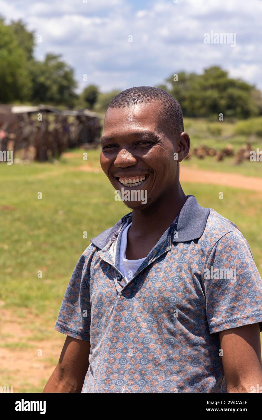 jeune homme africain dans le village debout sur la pelouse avec un grand sourire Banque D'Images