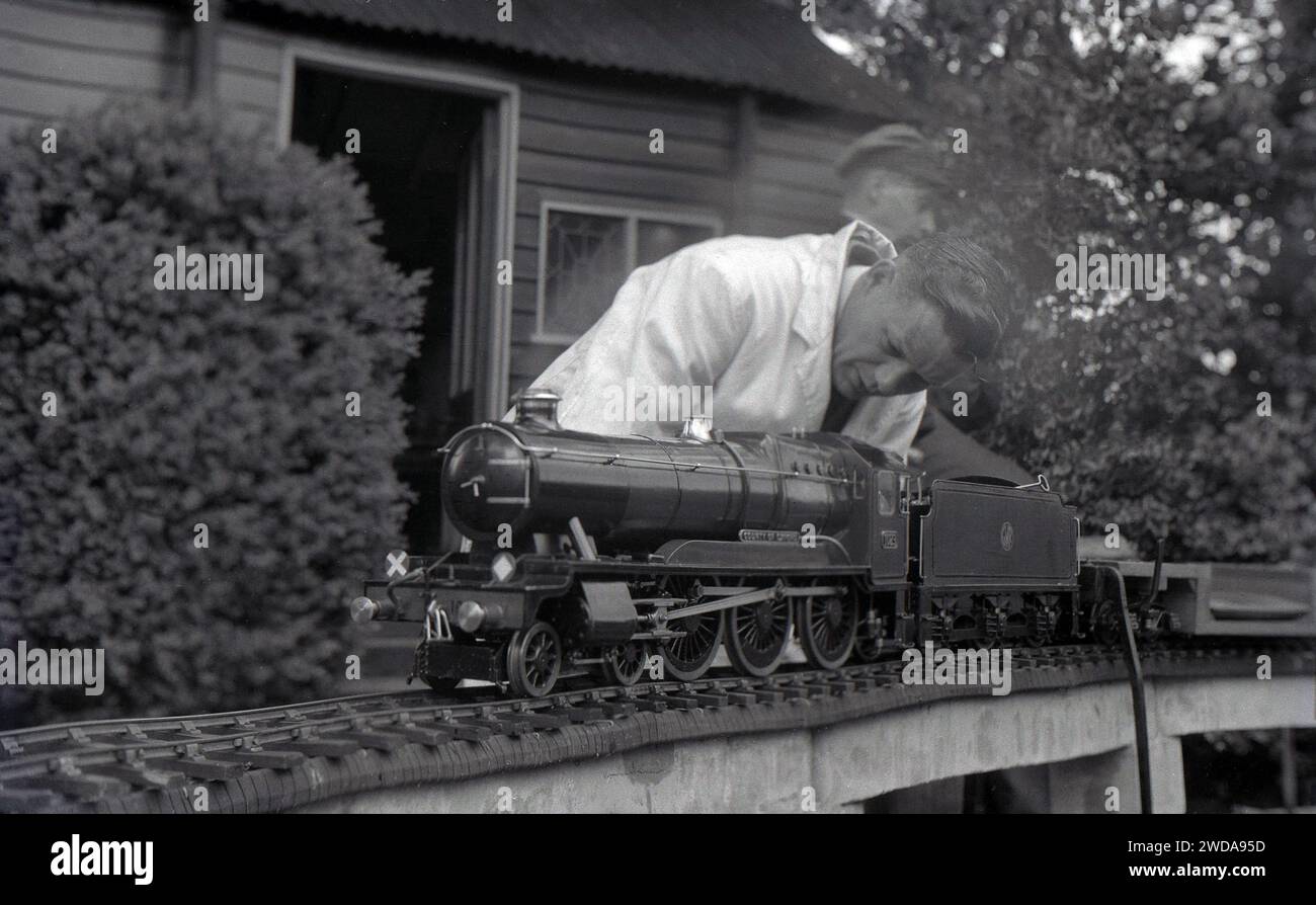 Années 1950, historique, à l'extérieur dans le jardin de la Field End Railway Co, Angleterre, Royaume-Uni, un passionné de modèle de chemin de fer à vapeur en blouse blanche travaillant sur un train à vapeur miniature, «County of Oxford», une locomotive à vapeur GWR qui est entrée en service en 1947. Banque D'Images